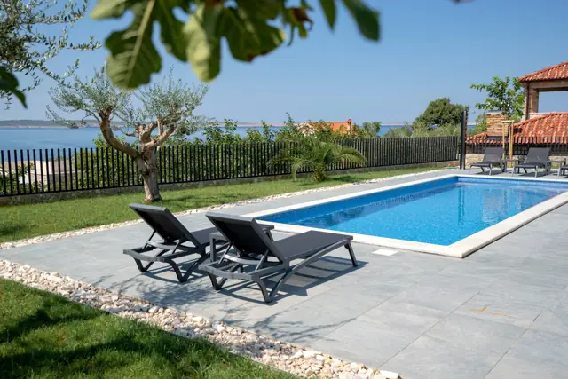 Sun loungers by the pool with olive trees and open sea view