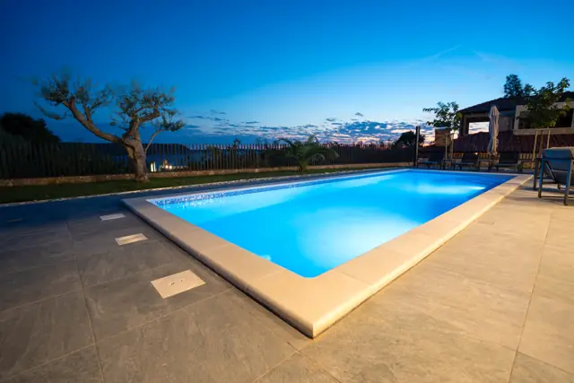 Illuminated private pool at dusk with olive tree and sea horizon