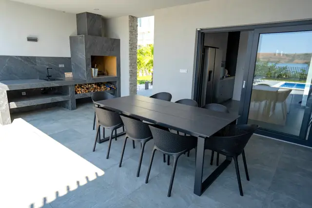 Covered outdoor kitchen with grill, dining table and pool view