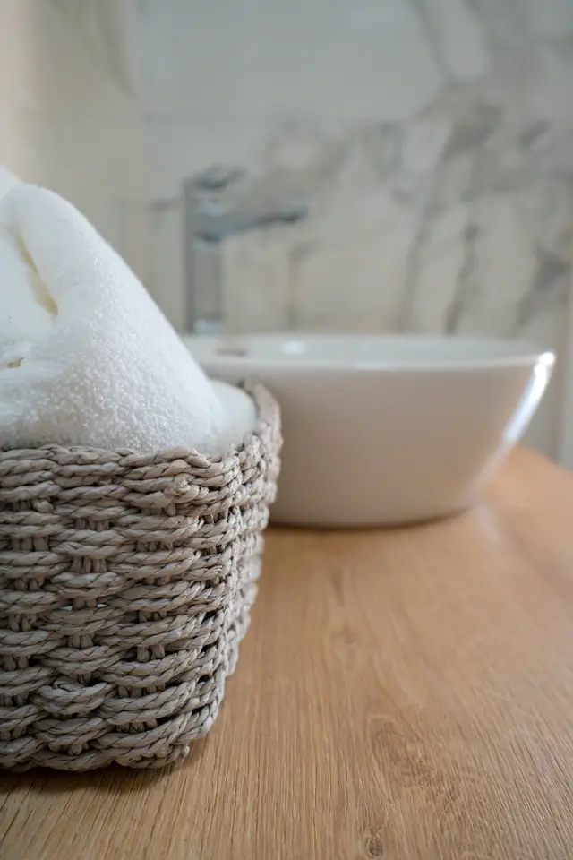 Rolled towels in a woven basket by the marble basin